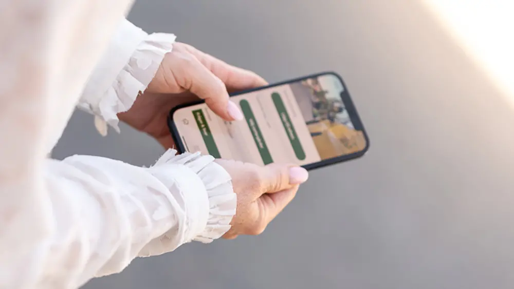 En person håller i en mobiltelefon med vår app på skärmen.