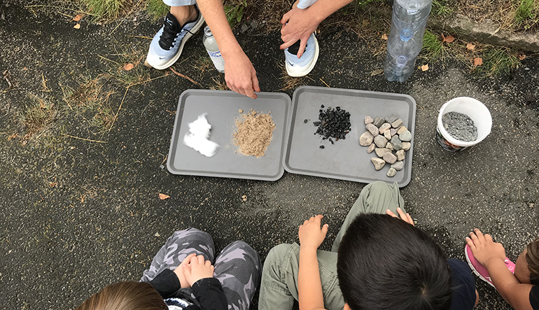 Barn framför en bricka med stenar, grus och sand.