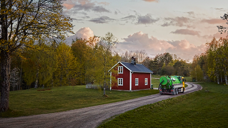 En slambil utanför ett rött hus på landsbygden.