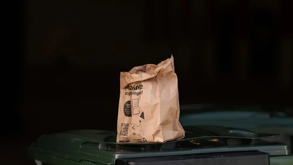 En matavfallspåse av papper är placerad på ett grönt sopkärl.
