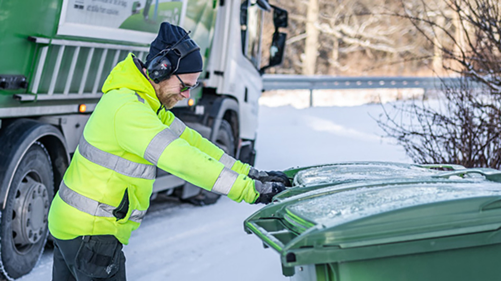 Sophämtaren kör ett sopkärl. I bakgrunden syns sopbilen.